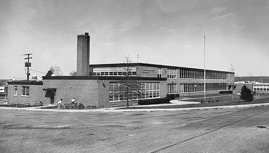 Black and white photograph of Churchill Road Elementary School. Two students are parking their bicycles next to the building.