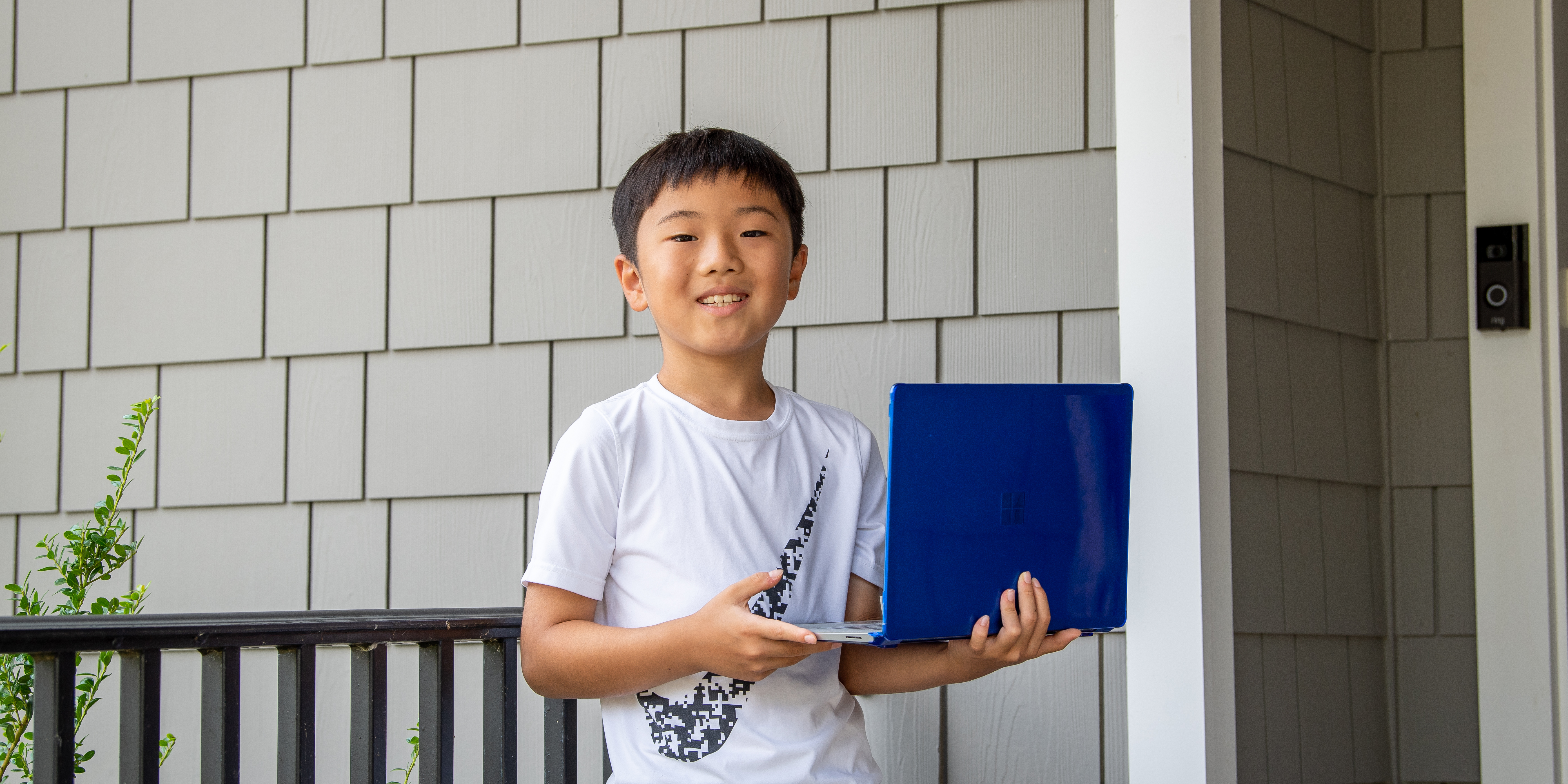 FCPS fourth-grader Ethan Zhang stands outside his home with his laptop.